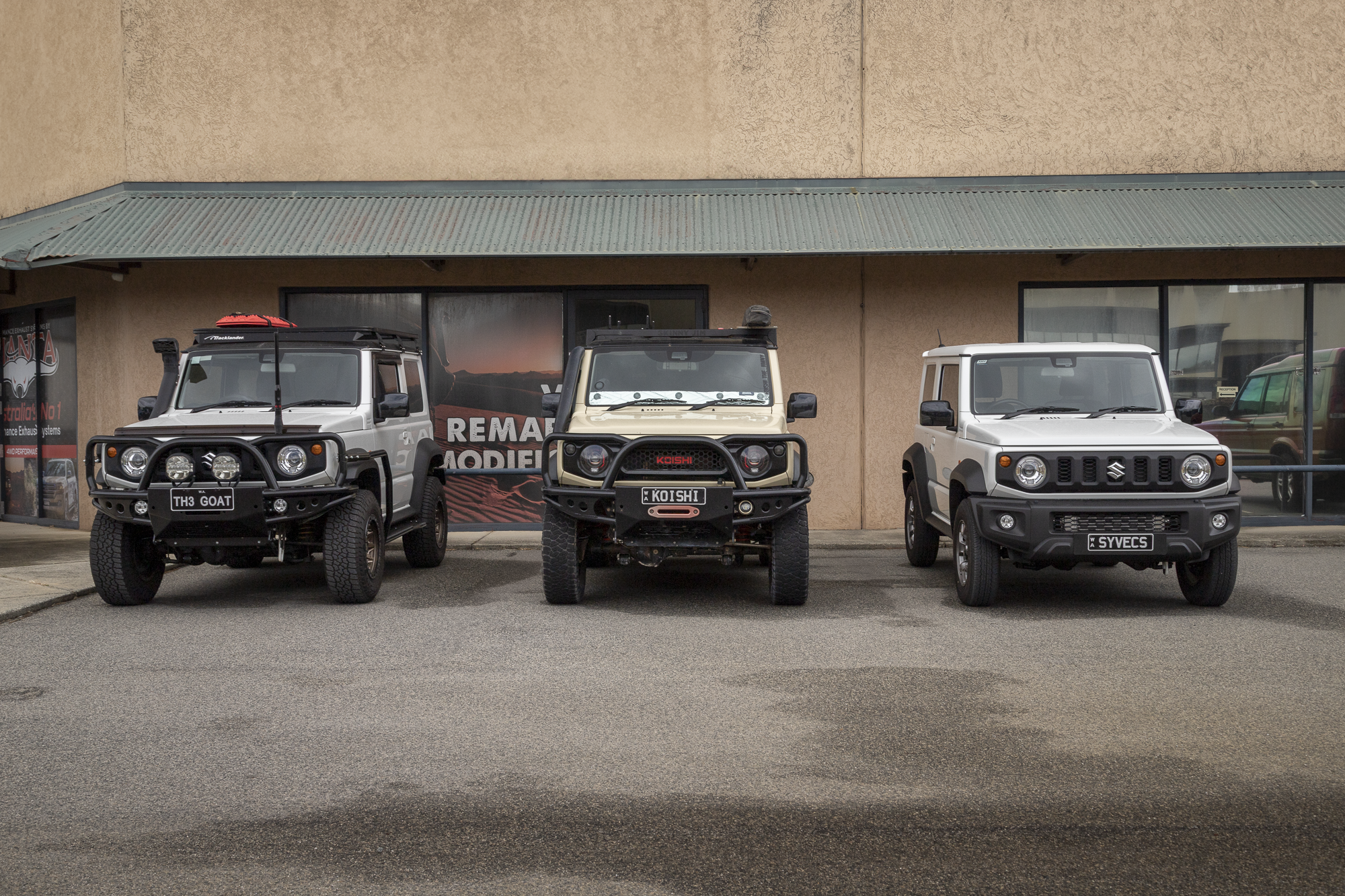 Three JB74 Suzuki Jimnys parked in a line in front of AMV Automotive. The vehicles have a number of modifications including Raslarr Barwork, Syvecs ECU, AMV Turbo kit, Harrop Supercharger, UCWS Window Shades, AMV Intercooler.