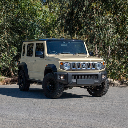 Chiffon Ivory/Sandy Suzuki Jimny XL JC74  parked in front of green leafy backdrop